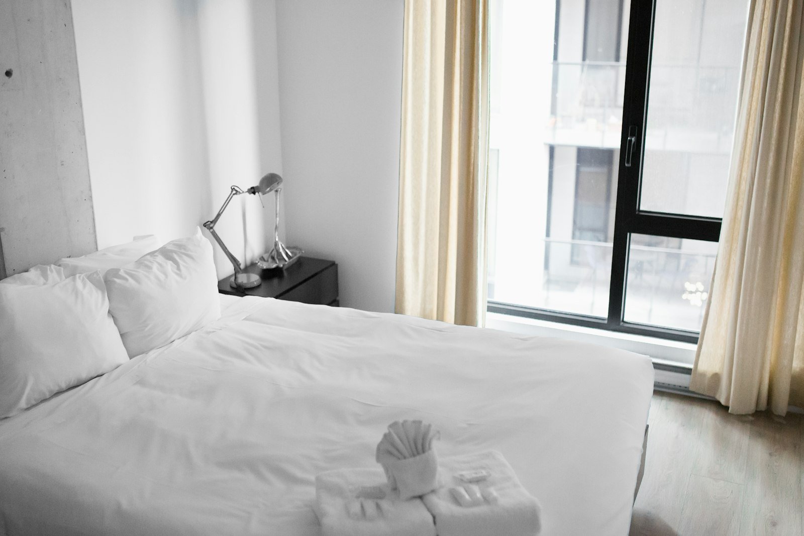 A freshly made bed with white linen beside a bright window